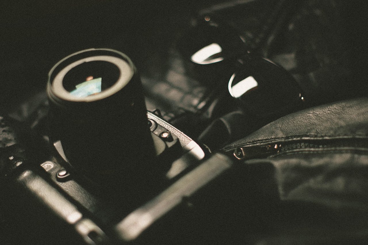 A digital camera with sunglasses on a black leather surface, exuding a stylish vibe.